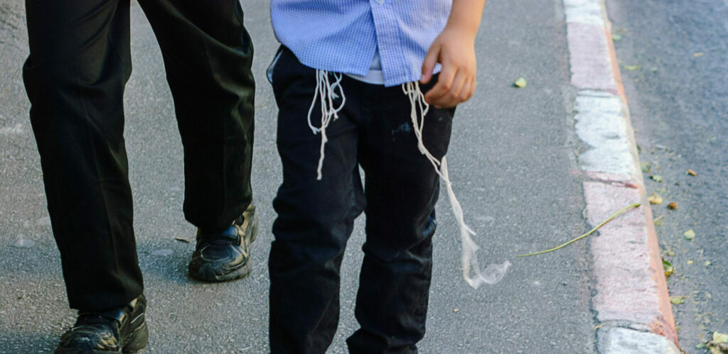 Religious Orthodox Jewish man and boy in traditional clothes and shabby shoe walk on Jerusalem street. Strings you see hanging out of their shirts are called tzitzit - specially knotted ritual fringes